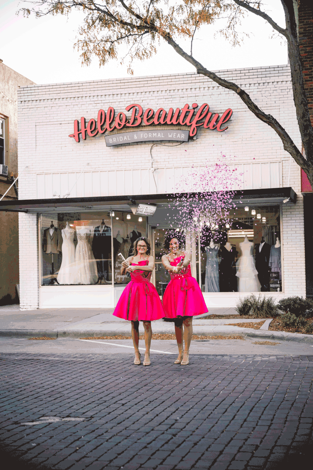 Two women in bright pink dresses standing outside Holly Beautiful boutique