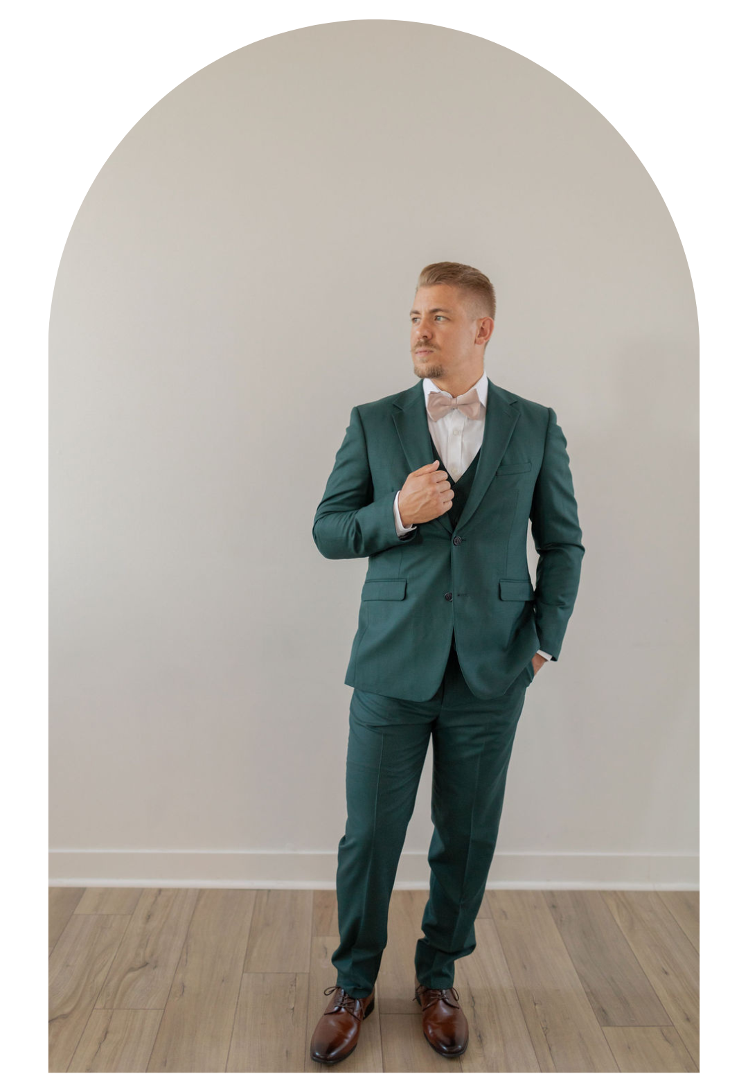 Man in green suit standing in an arched alcove, adjusting his jacket on a wood floor.
