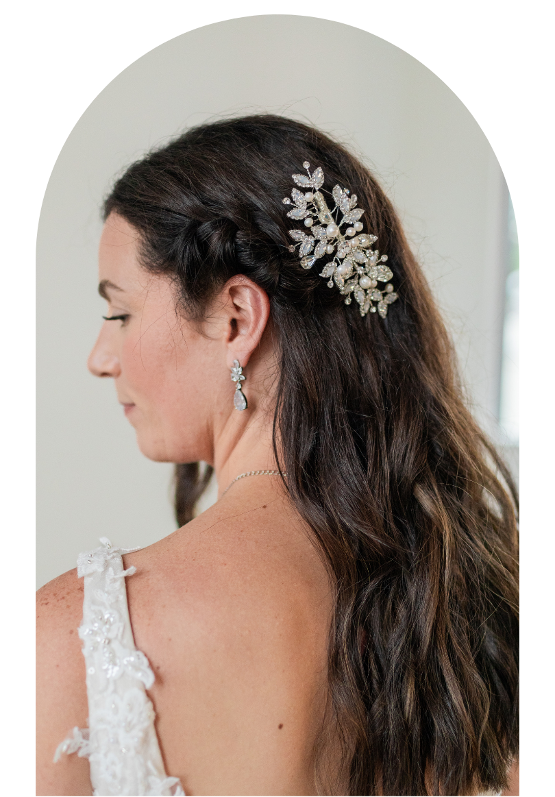 Profile view of a woman with long dark hair wearing a jeweled hair accessory and earrings against a light background