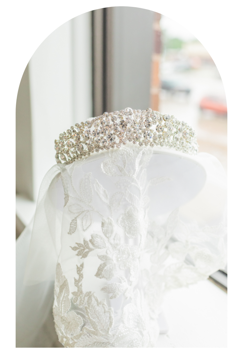 White lace bridal veil with a jeweled tiara, hanging by a window