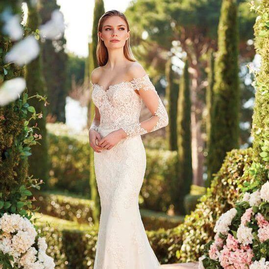 Woman in an ivory lace gown standing in a flower-lined garden path