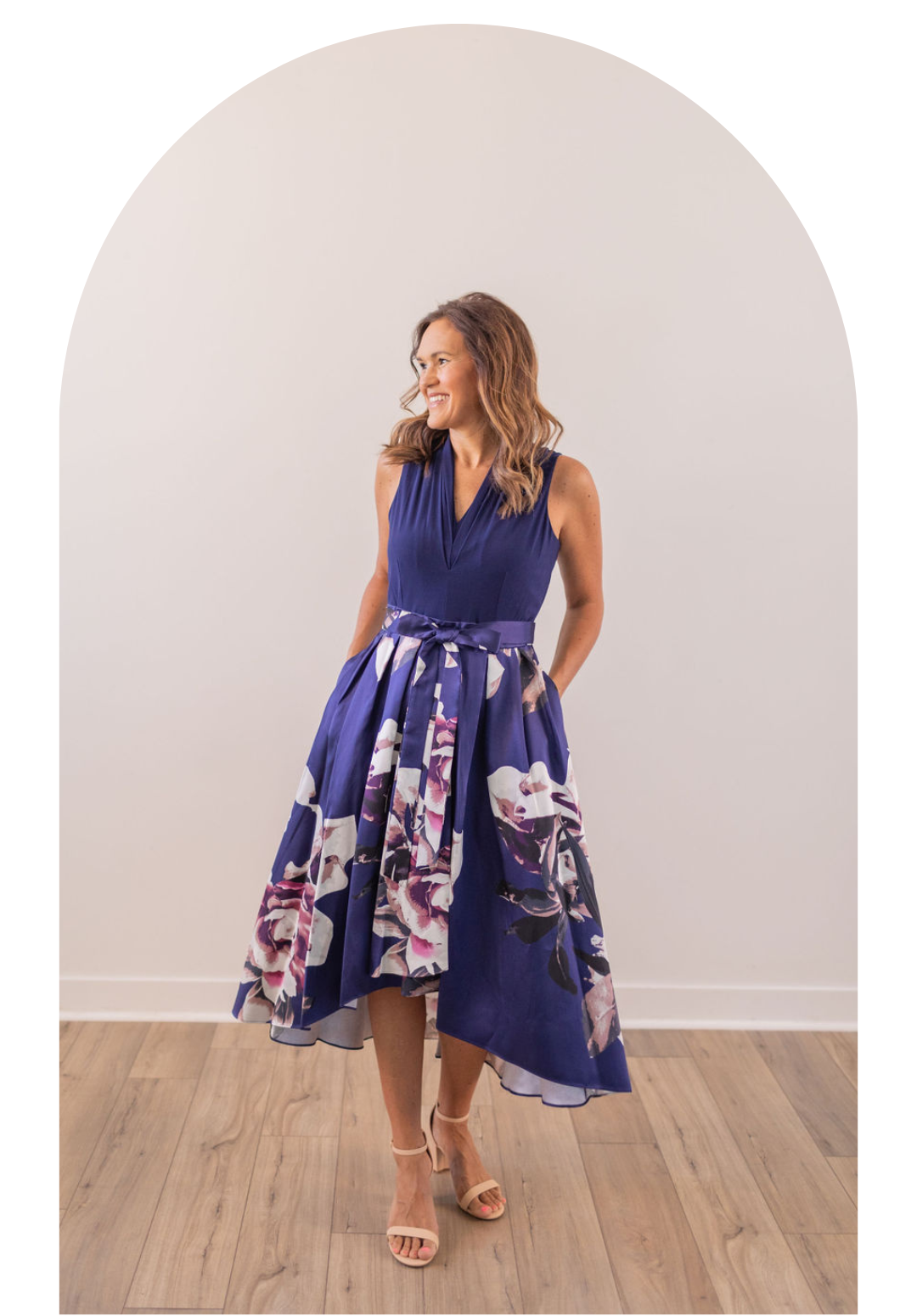 Woman in a navy floral dress posing in a bright room with wood flooring