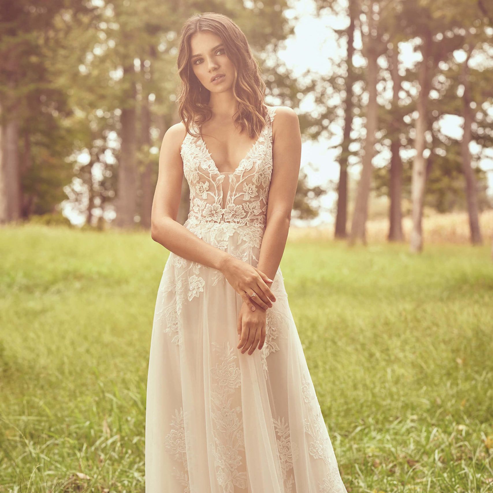 Woman in a white lace dress standing in a sunlit grassy field among trees