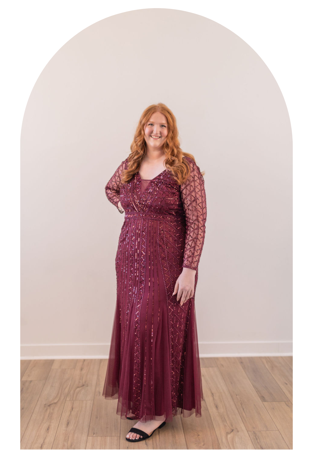 Woman in a burgundy sequined dress posing indoors against a white arched wall.