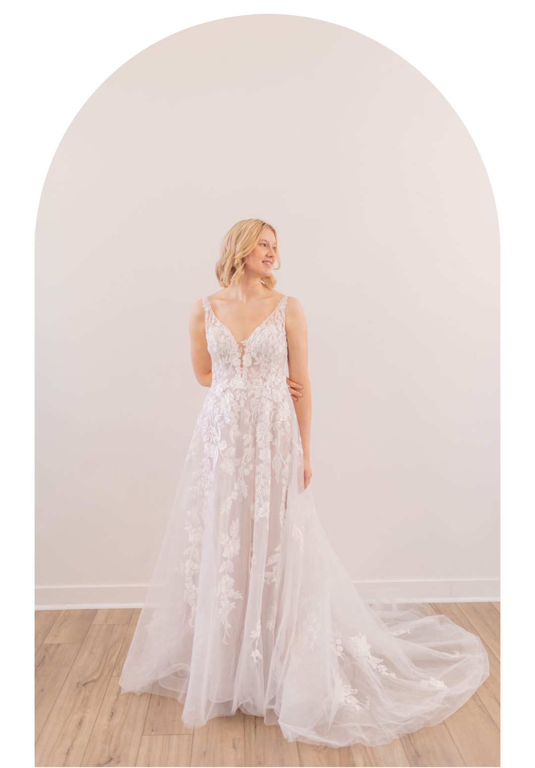 Woman in a white lace wedding gown standing in a bright room with a flowing train