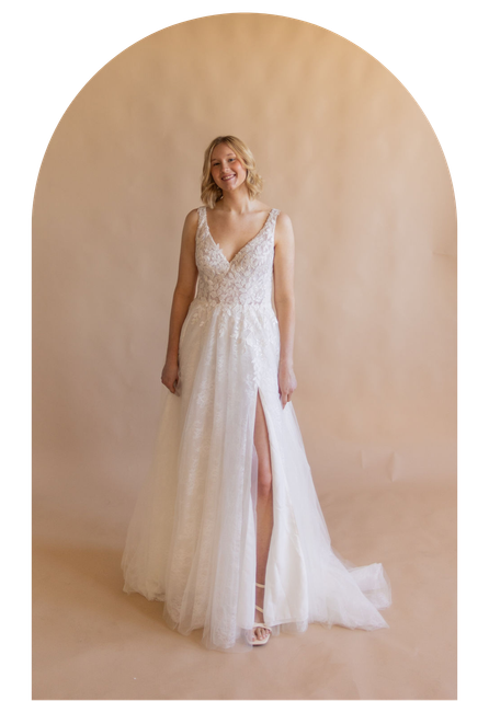 Bride in a white lace wedding gown standing before a soft beige backdrop