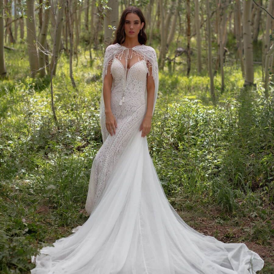 Woman in a white lace wedding dress standing in a wooded forest clearing