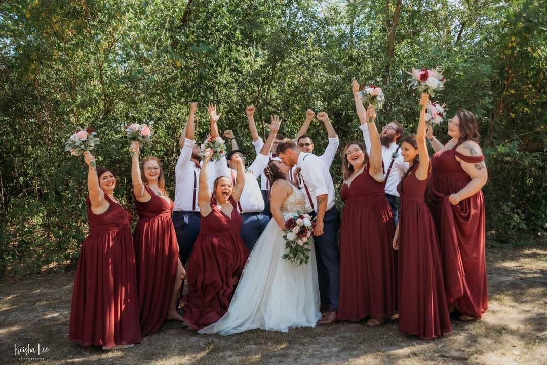 Bride and bridesmaids in burgundy dresses cheering outdoors among trees