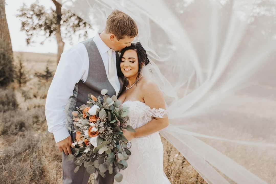 Bride and groom embracing outdoors, with flowing veil and bouquet in soft light