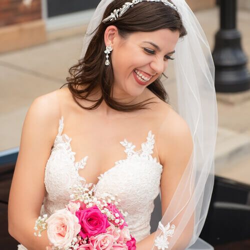 Bride in a white lace dress smiling and holding a pink and white bouquet