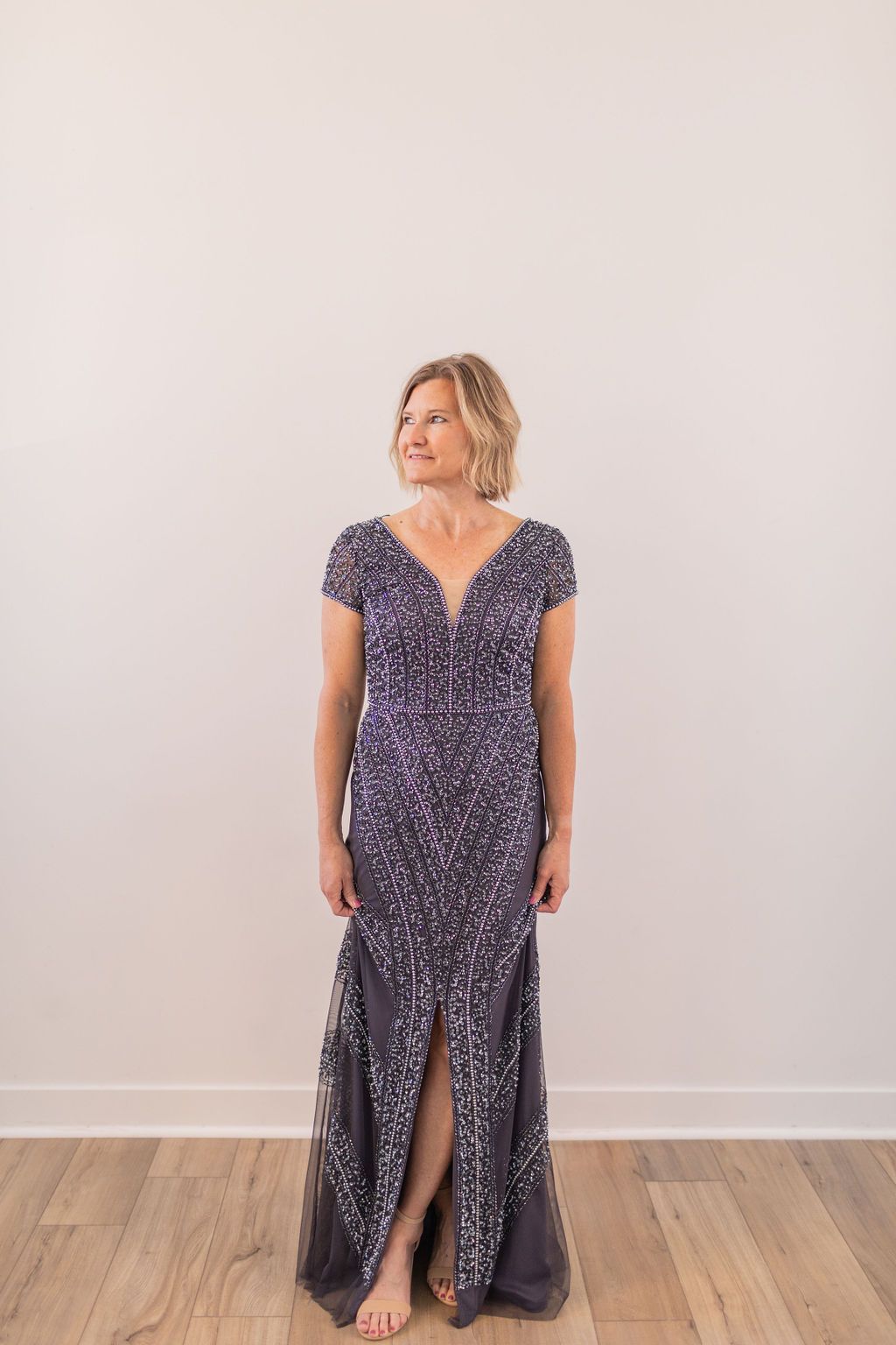 Woman in a burgundy sequined gown standing against a plain white wall and wood floor