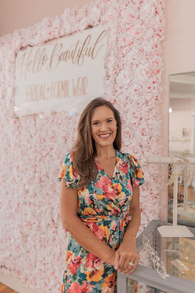 Woman in a floral dress standing before a pink flower wall and sign at an event