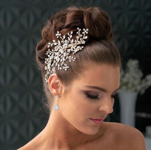Woman with an elegant updo and jeweled hair accessory, looking down in a softly lit indoor setting