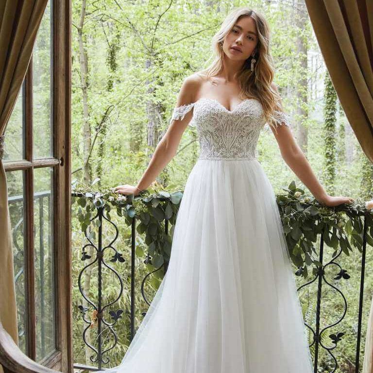 Bride in a white lace gown standing on a balcony with a lush green forest behind her