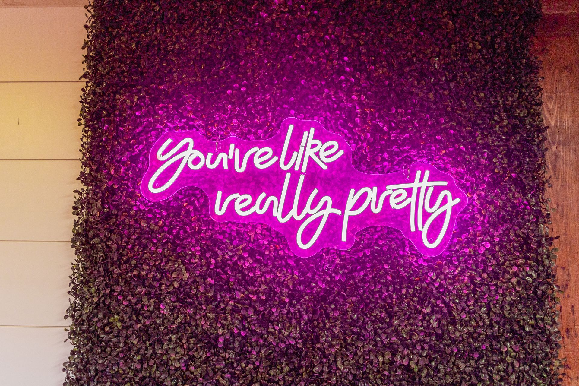 Neon pink sign reading “you’re like really pretty” on a dark glittery wall