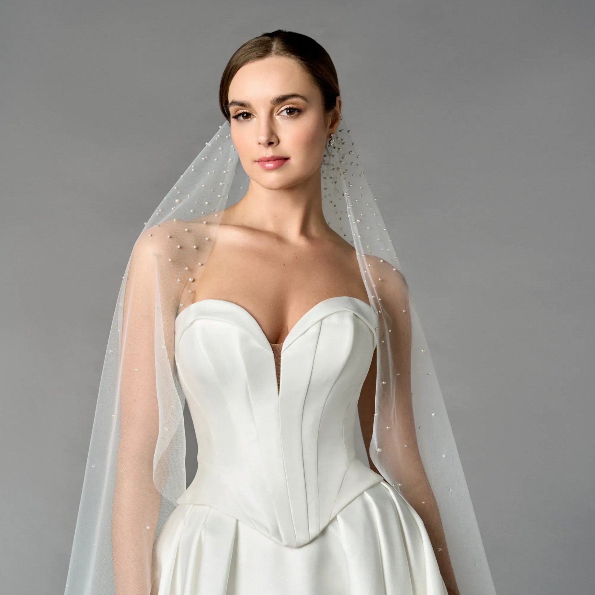 Bride in a strapless white wedding gown with a sheer veil against a gray background