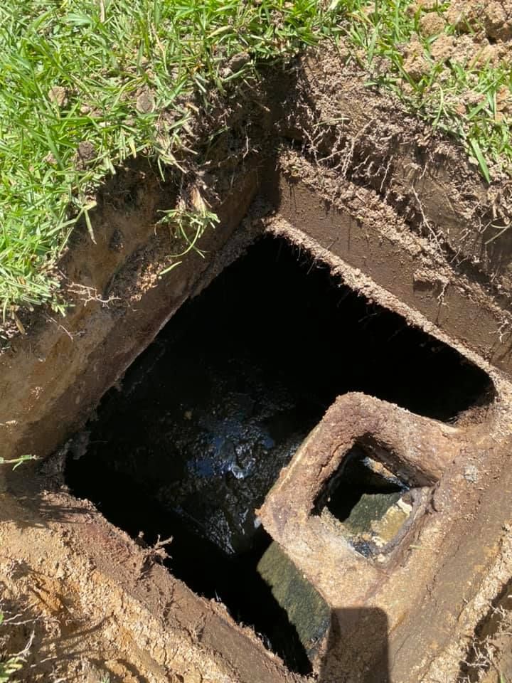 A manhole cover is sitting in the dirt next to a grassy area.