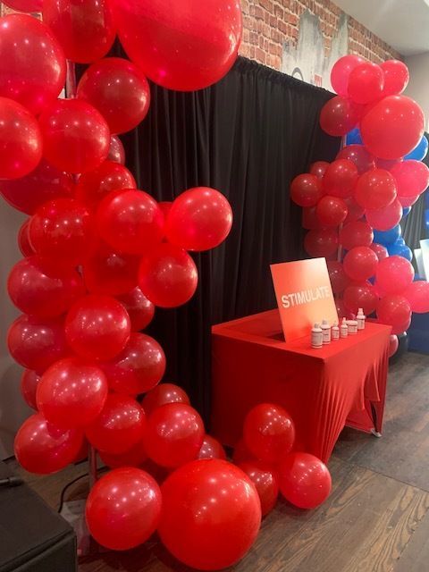 Red balloon arch framing a red table with a sign at an event booth indoors