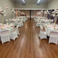 Decorated banquet hall with round tables, white chair covers, and floral centerpieces around a wood dance floor