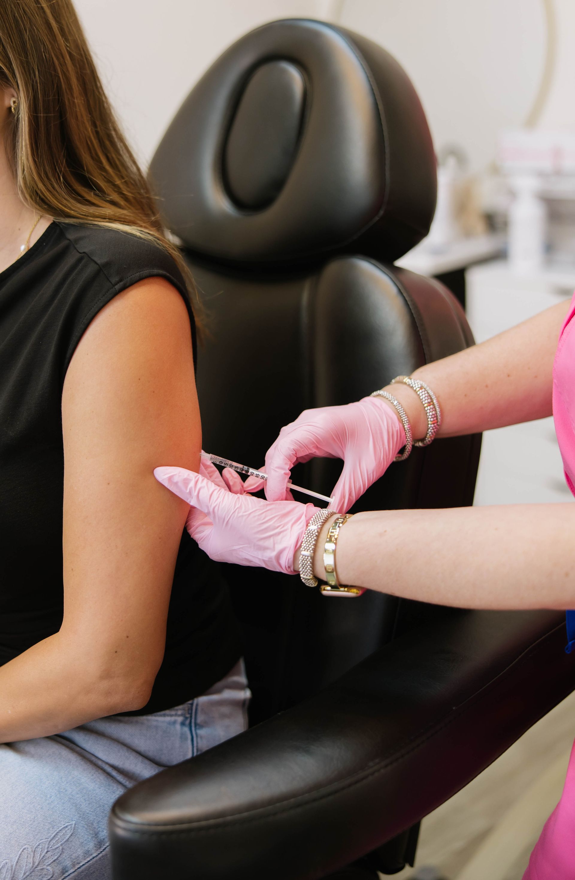 Client getting treatment while a technician in pink gloves works on their hand in a salon chair