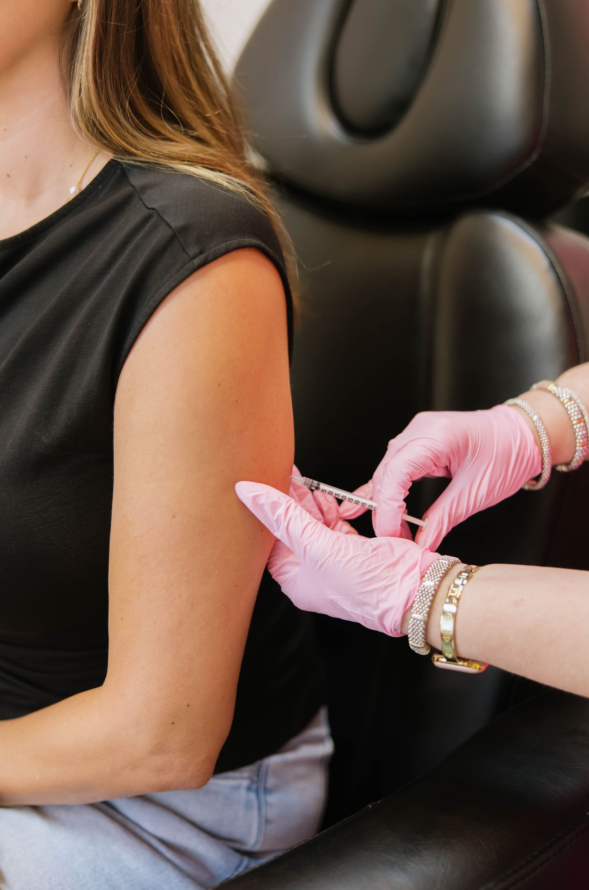 Pink-gloved hands fastening a bracelet on a seated person's arm in a car seat