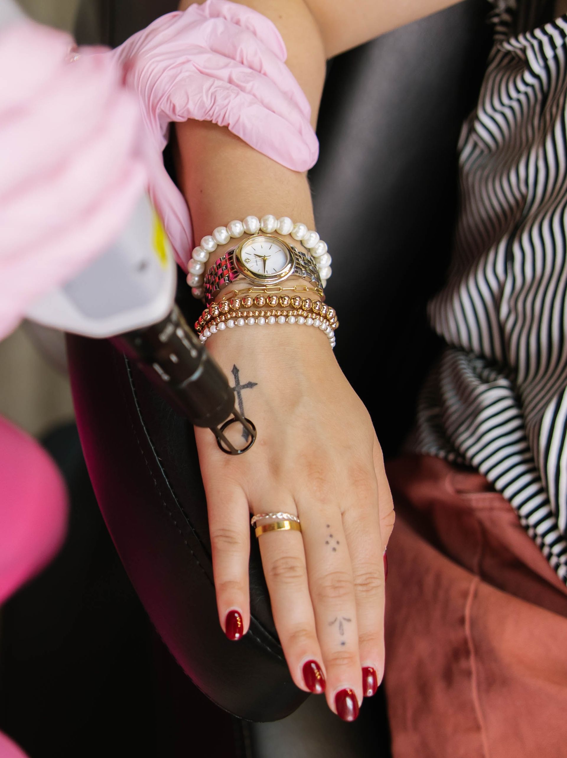 Hand with red nails and bracelets, held by a gloved person in a striped shirt and pink skirt