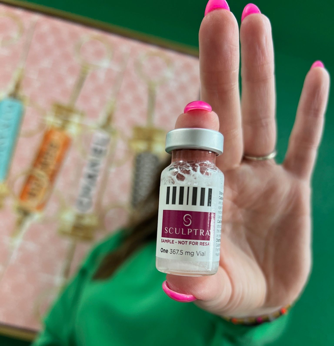 Hand holding a small medical vial with pink label and cap against a green background.
