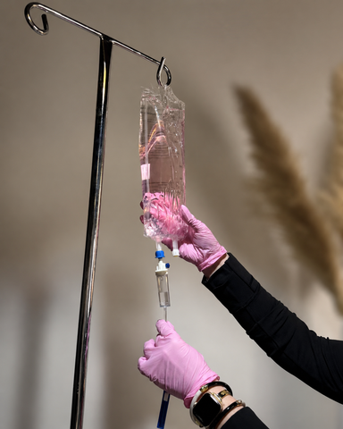 Gloved hands adjust a pink IV drip bag hanging from a metal stand