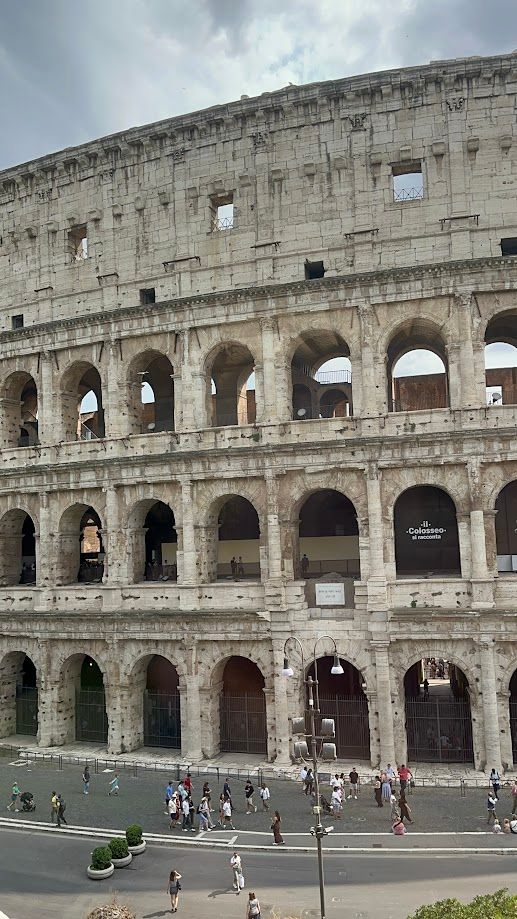 Roman Colosseum exterior with tourists walking below under arched stone levels