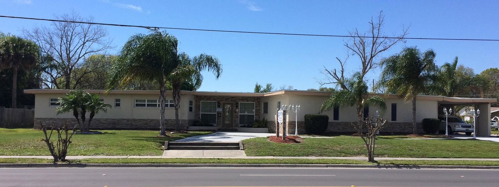 Single-story beige building with a central entrance, trees, and a lawn under a clear blue sky.