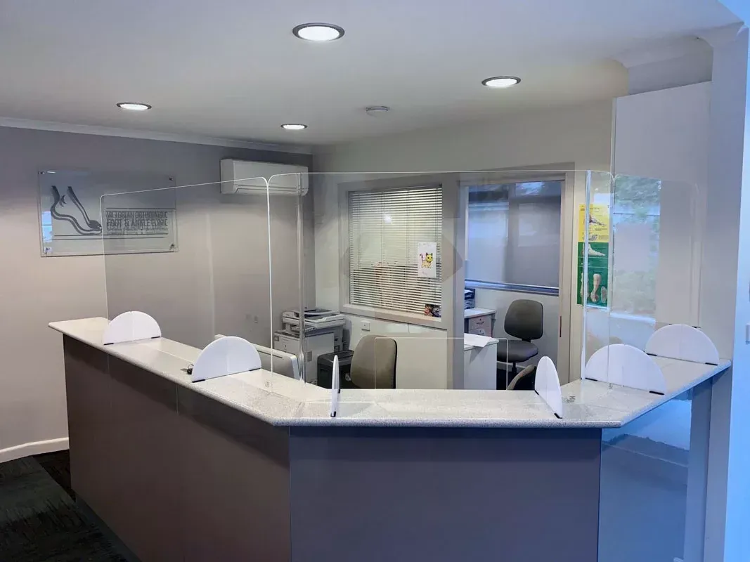A reception desk with a clear glass shield on it.