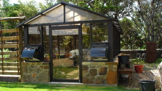 A greenhouse is sitting in the middle of a lush green yard.