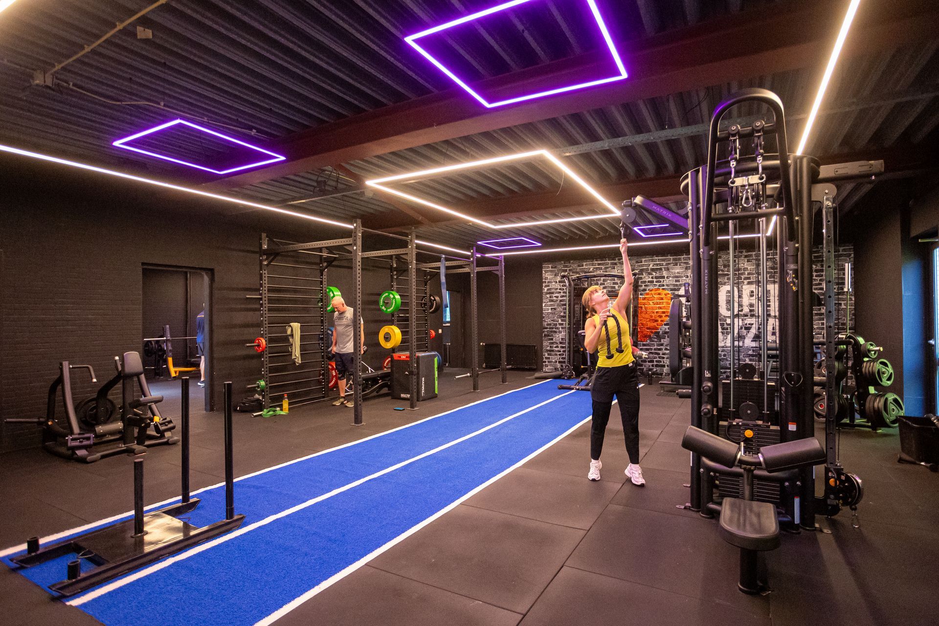 Een vrouw doet oefeningen in een sportschool met paarse lichten.