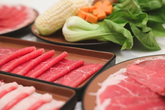 Trays of sliced beef and vegetables on a table, prepared for hot pot cooking