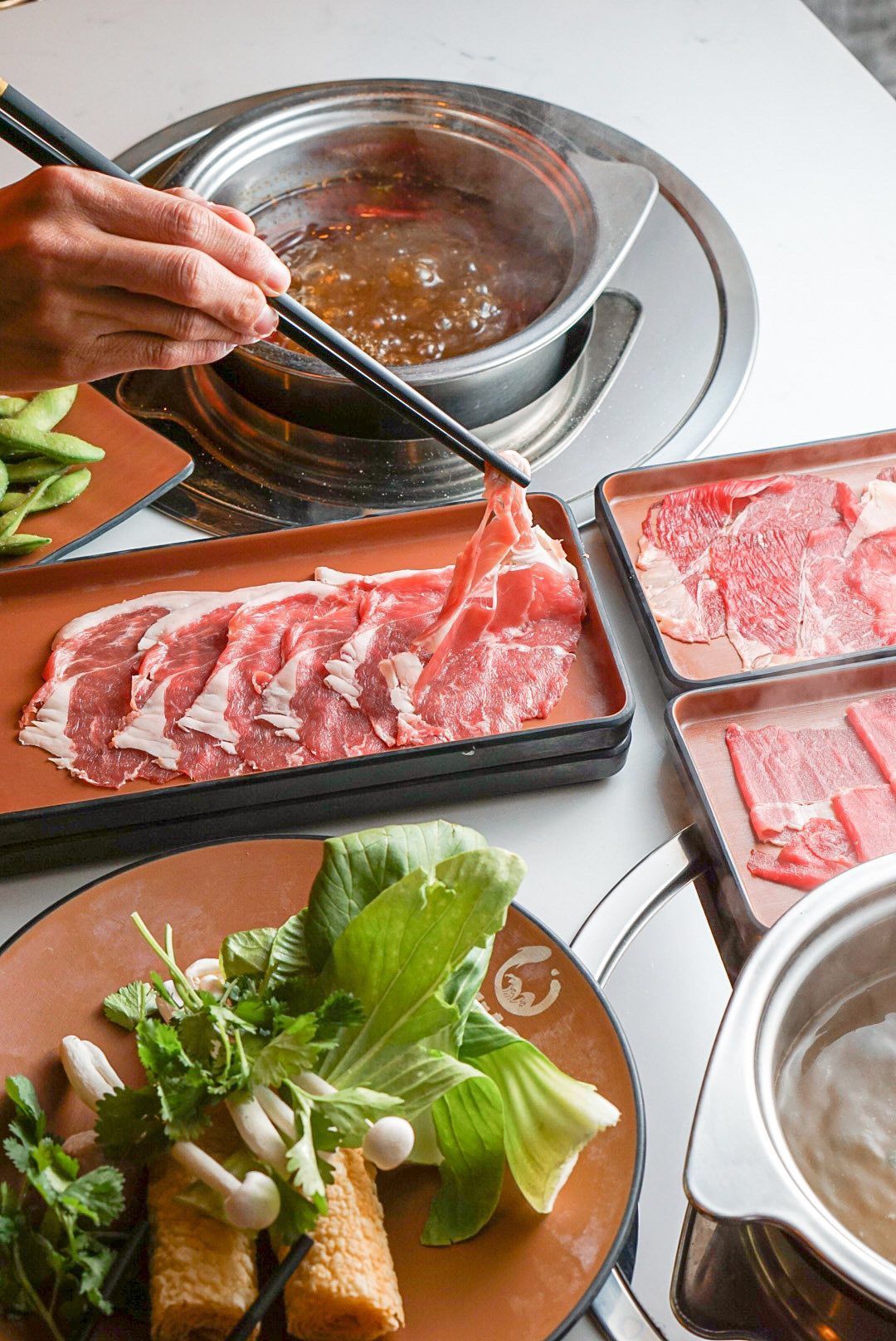Japanese hot pot with raw beef, vegetables, and chopsticks over a simmering metal pot