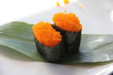 Two bright orange sushi roe gunkan rolls on a green leaf-lined plate