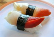 Two pieces of sushi nigiri with white rice, white fish, and red topping on a white plate