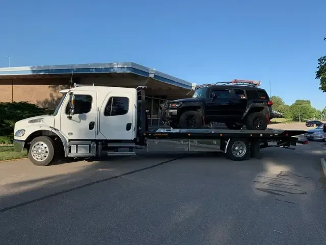A tow truck is carrying a black suv on the back of it.