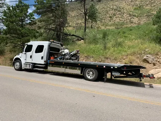 A tow truck with a motorcycle on the back is parked on the side of the road.
