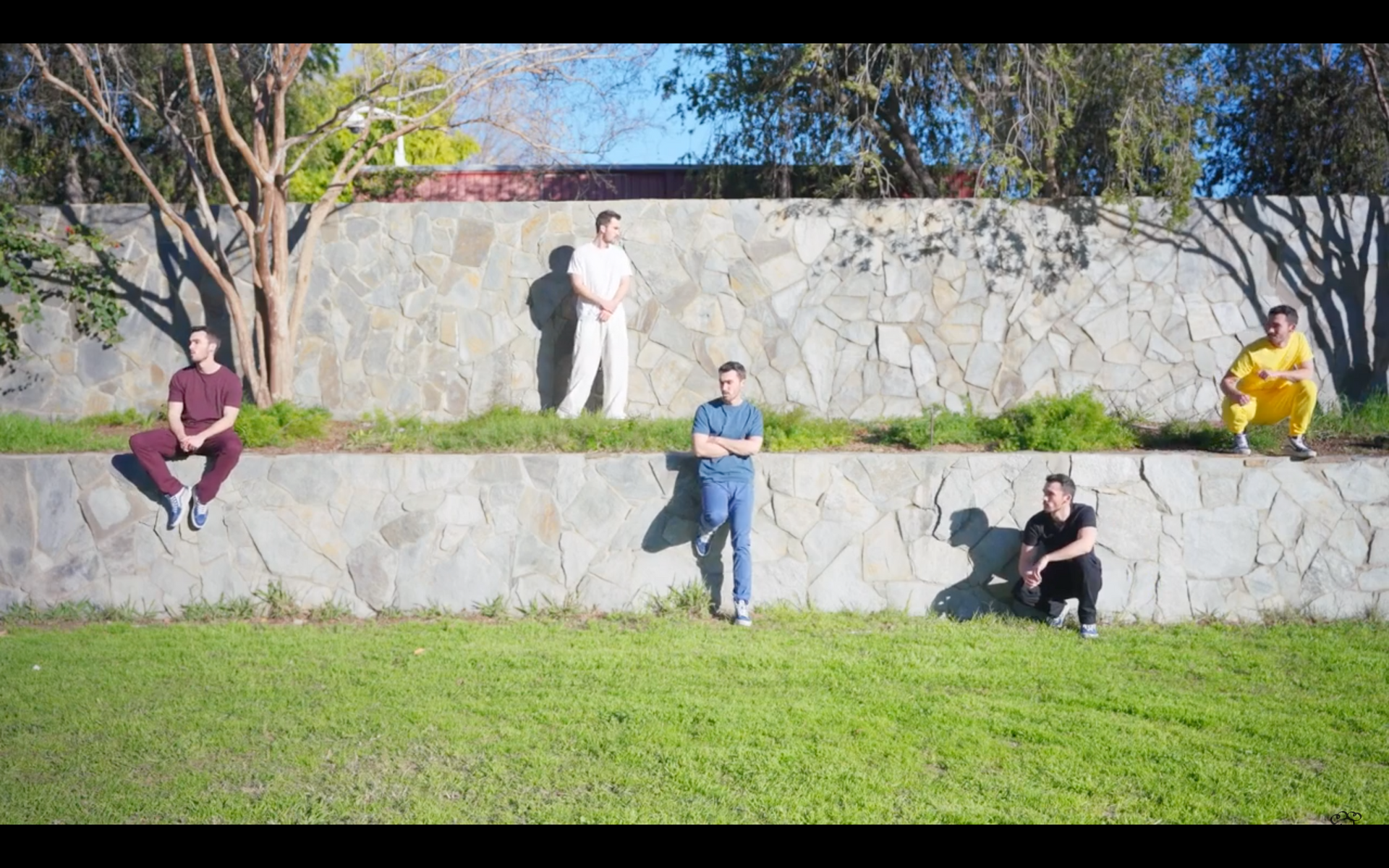 A group of men are standing in front of a stone wall in a park.