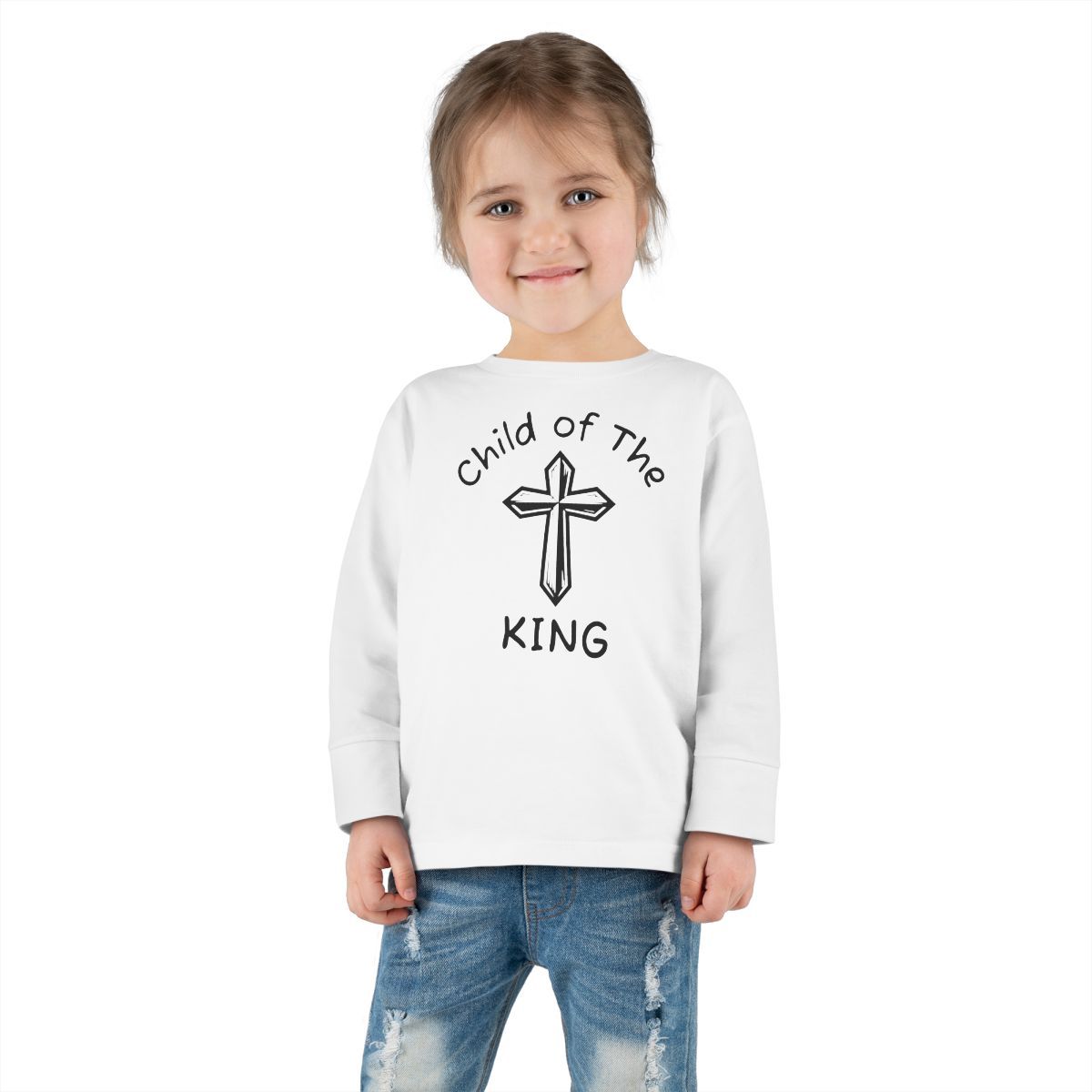 A young child wearing a white long-sleeved shirt with "Child of the King" and a cross graphic.