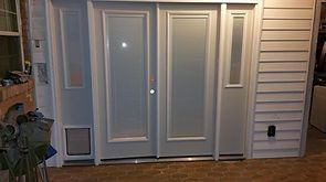 Exterior double doors, sidelight, and pet door in a light-colored frame. The building has light siding and brick flooring.