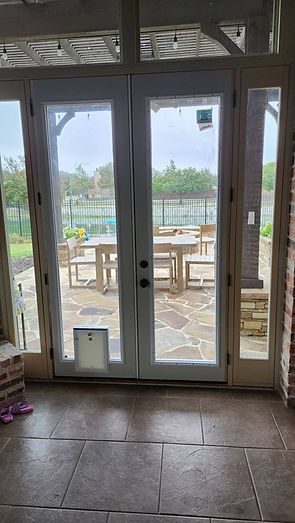 Glass doors with a pet door, leading to a patio with tables, chairs, and a yard.