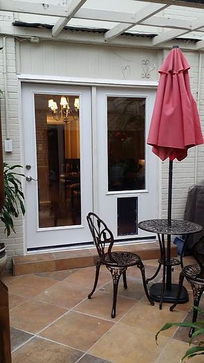 White double doors with a pet door, opening onto a patio with furniture and a red umbrella.