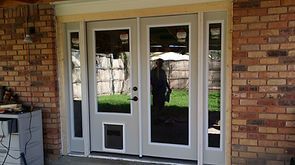 Double glass doors with sidelights in a brick building. One door has a pet door.