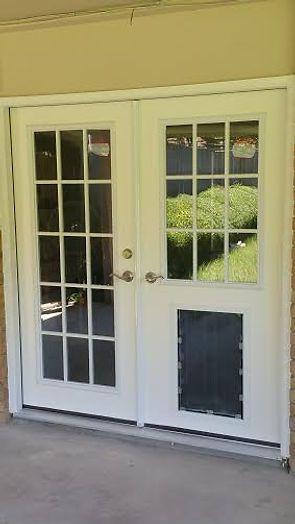White double doors with glass panes and a dog door, set against a light-colored building exterior.