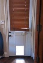 White door with wooden blinds and a pet door, set in a wood-framed doorway.