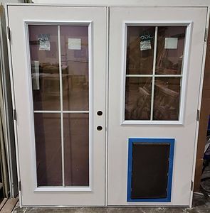 White French doors, one with a pet door, with glass panels and grids, in a warehouse setting.