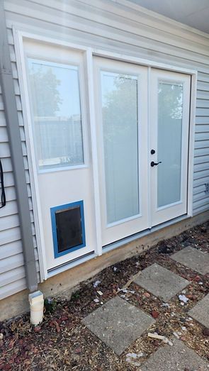 Exterior view of a white door with two glass panels and a window with a pet door; gray siding.