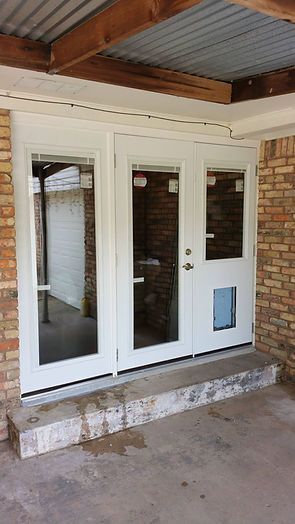 White French doors with dog door, on concrete step, under corrugated roof, brick wall.